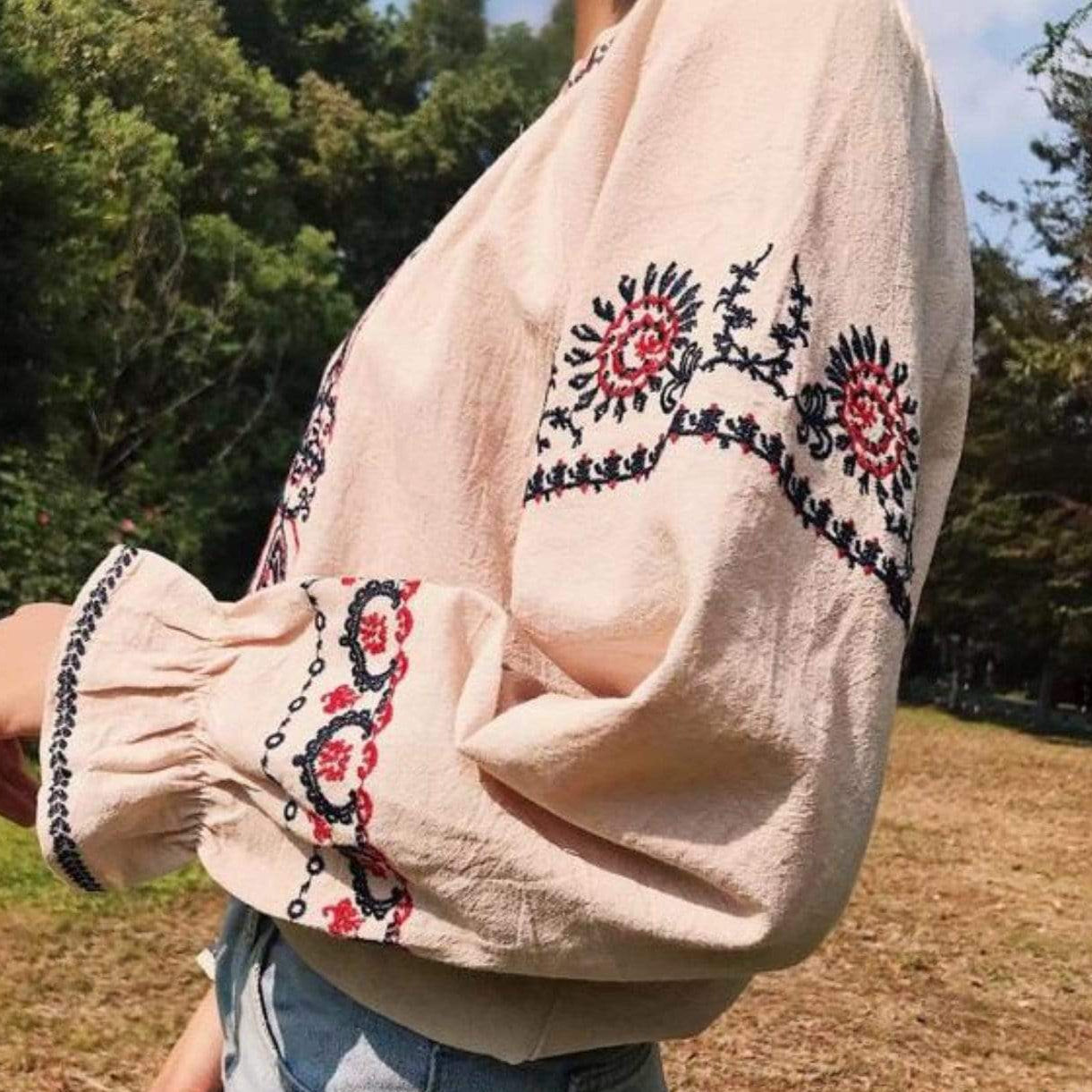 Person wearing a light pink blouse with floral embroidery and blue jeans outdoors.