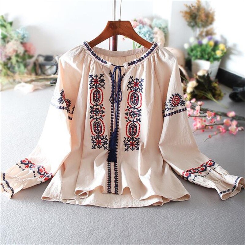 Beige blouse with red and blue embroidery hanging on a wooden hanger.
