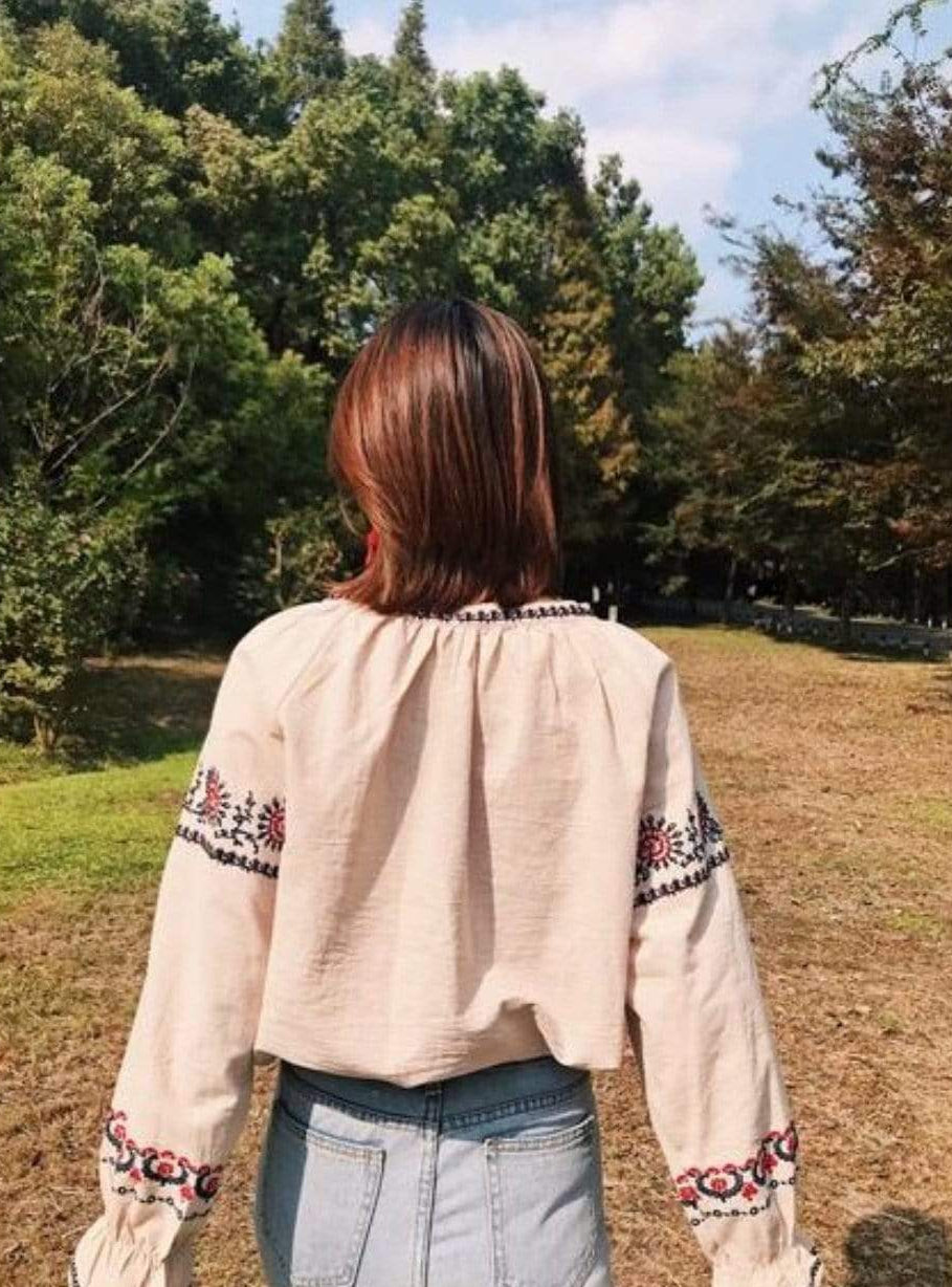 Back view of a woman wearing a tan embroidered blouse and light wash jeans outdoors.