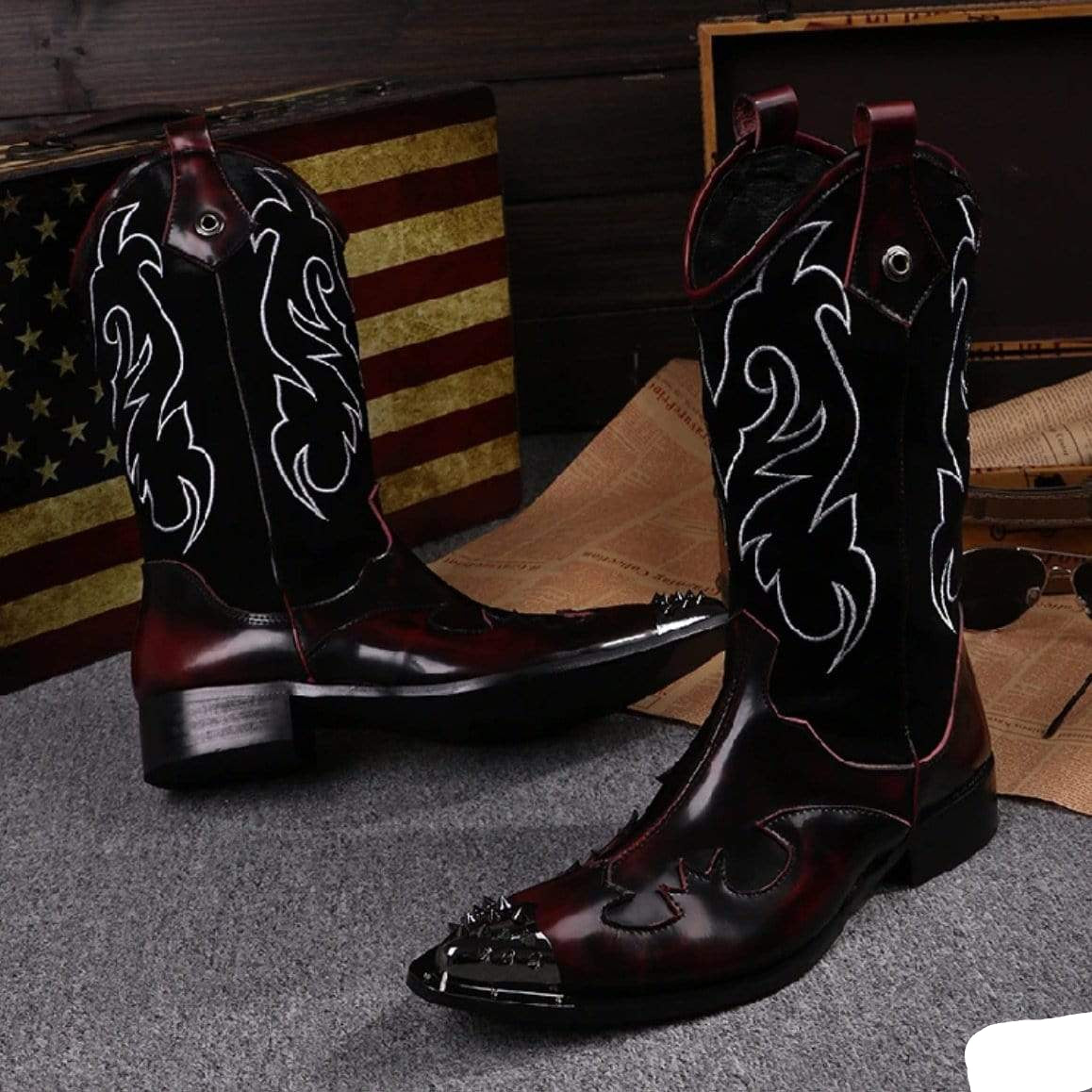 Pair of dark red and black leather cowboy boots with silver embellishments and white detailing, displayed on a gray surface.