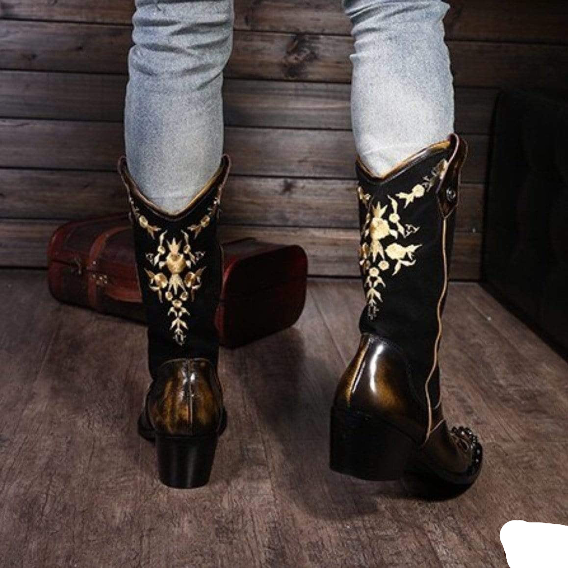Person in light grey jeans wearing black leather cowboy boots with gold embroidery.
