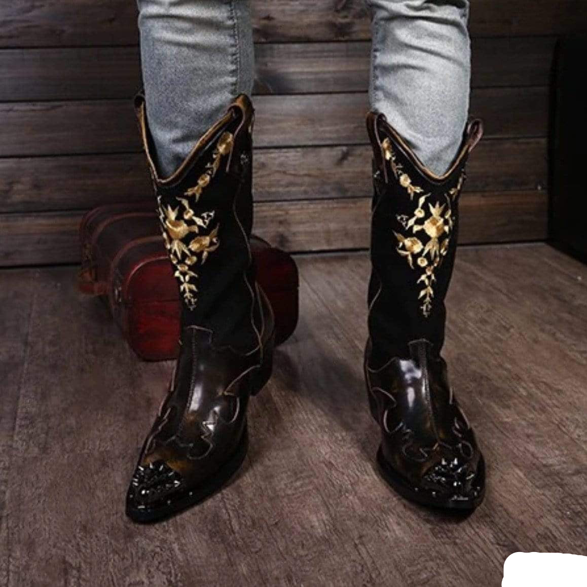Person wearing black leather cowboy boots with gold embroidery.