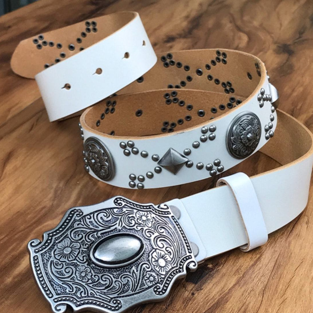 A white leather belt with a silver buckle and silver embellishments on a wooden surface.