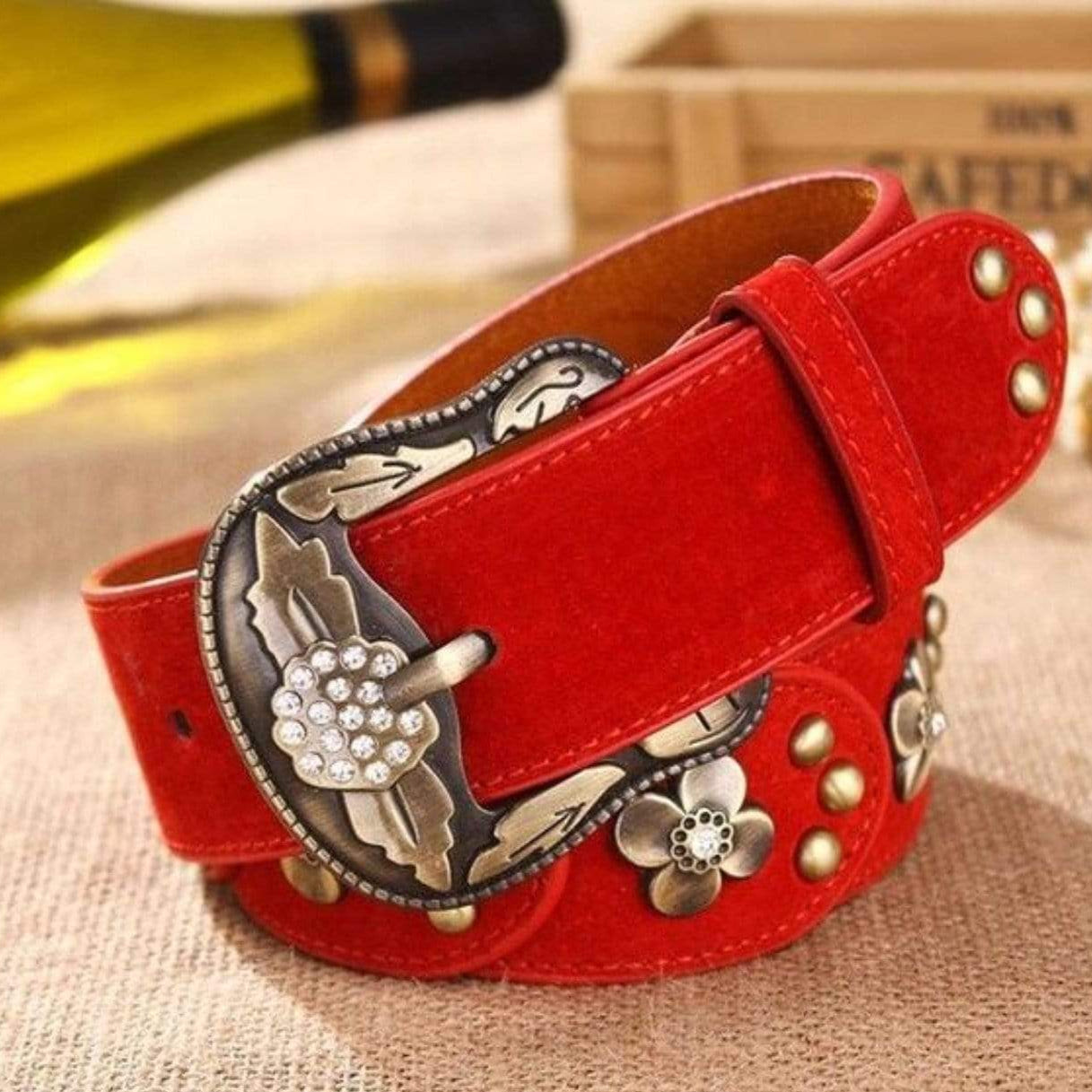 Close-up of a red suede belt with a large decorative metal buckle and floral embellishments.