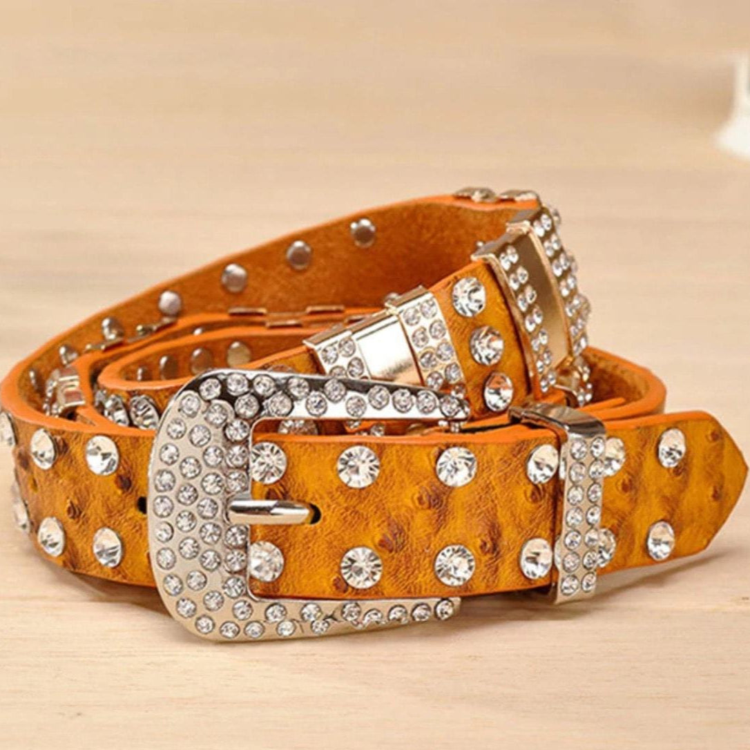 An orange leather belt with rhinestone decorations, displayed on a light wooden surface.