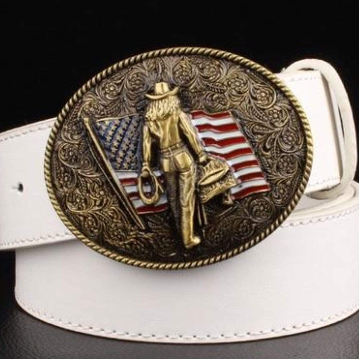 A white belt with a large, decorative bronze-colored buckle featuring a cowgirl figure and the American flag.
