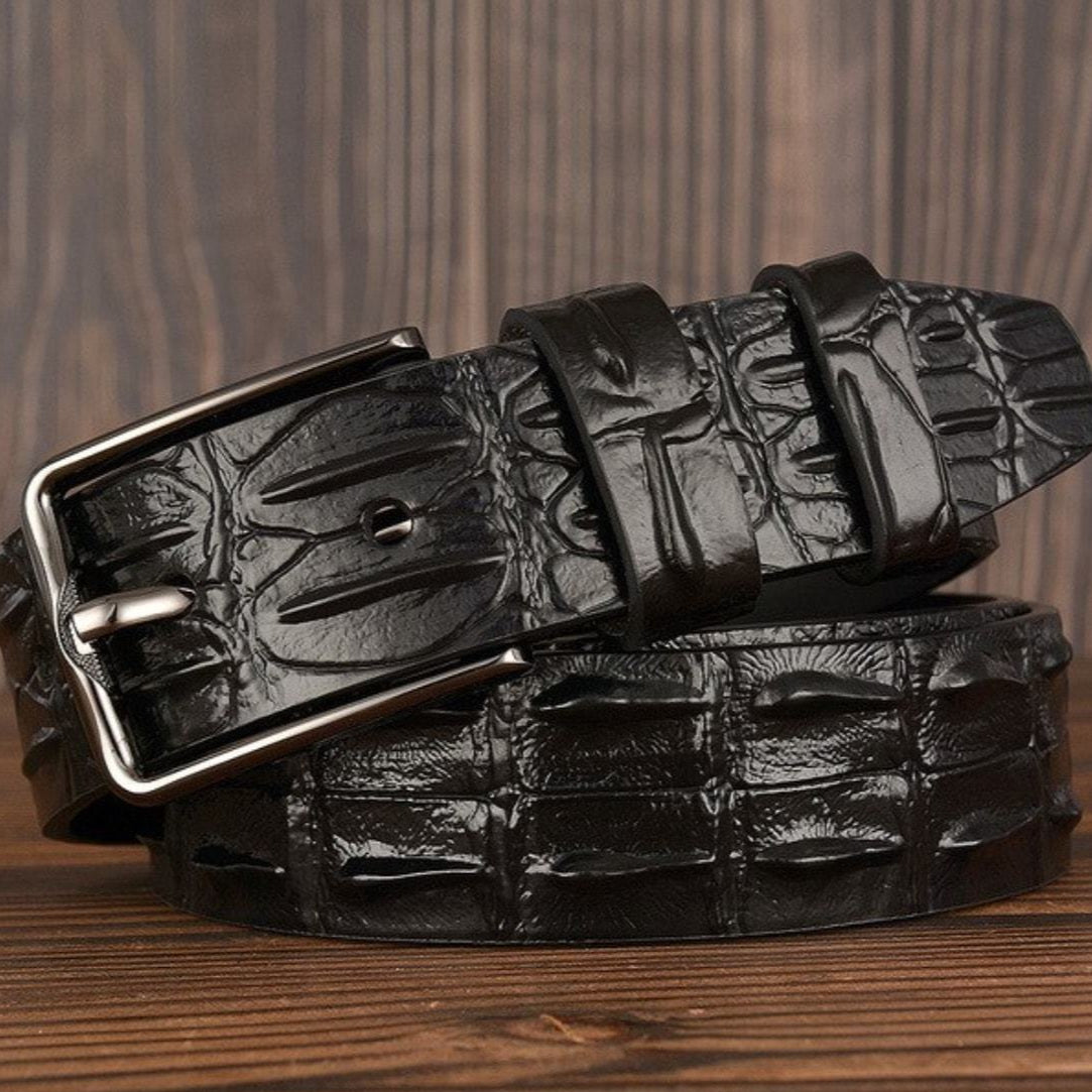 Black crocodile pattern belt with silver buckle on wood surface.
