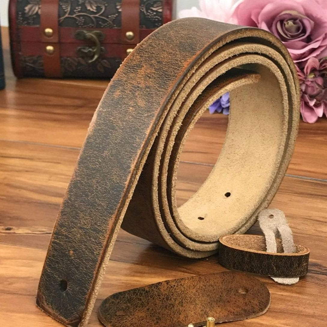 A brown leather belt with its buckle, loop, and fasteners laid out on a wooden surface with flowers and a treasure chest in the background.