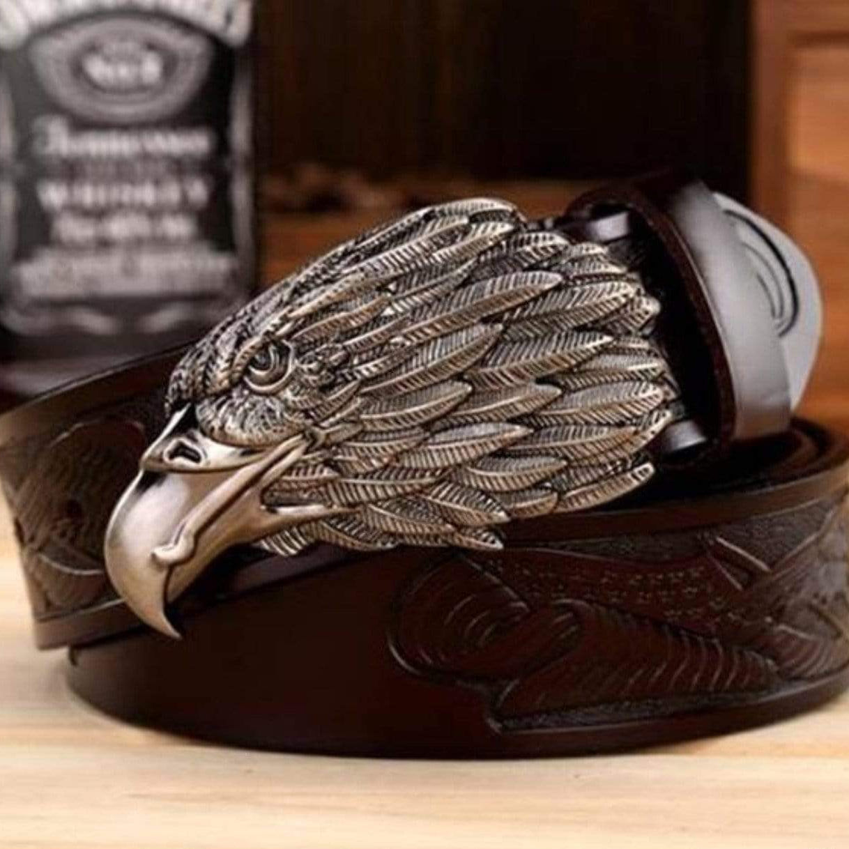 A brown leather belt with an eagle head buckle on a wooden surface. 
