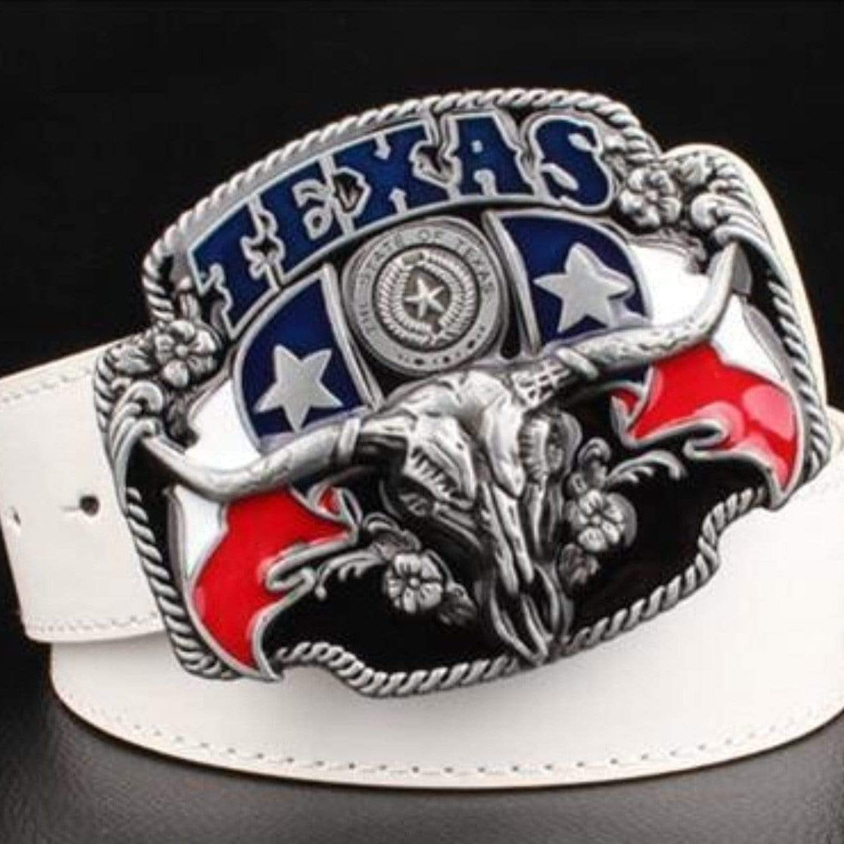 Close-up of a white leather belt with a large silver belt buckle featuring the word "TEXAS" in blue letters, the state seal, stars, and a steer skull on a black, white, and red background.