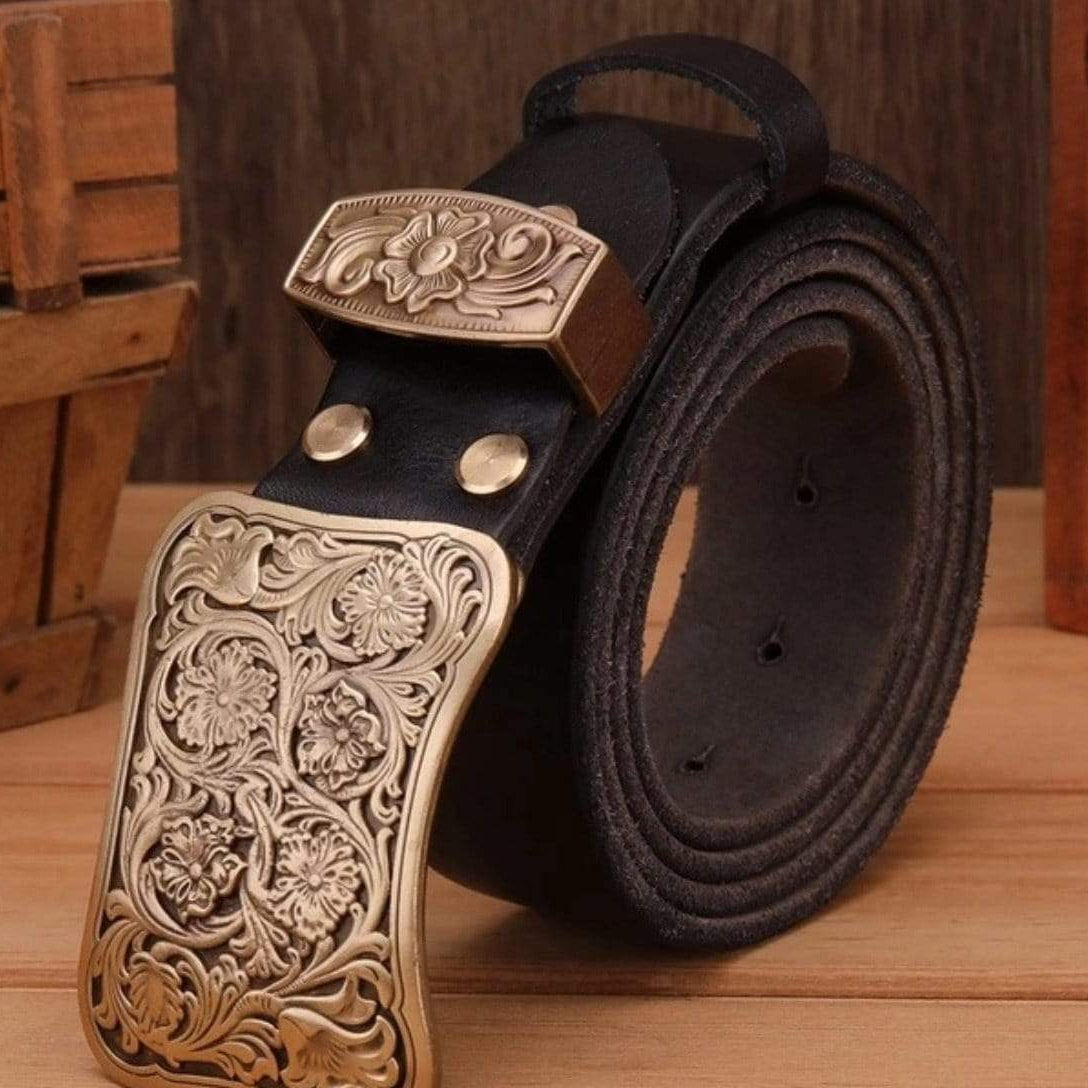 Black leather belt with large gold floral buckle on wooden surface.