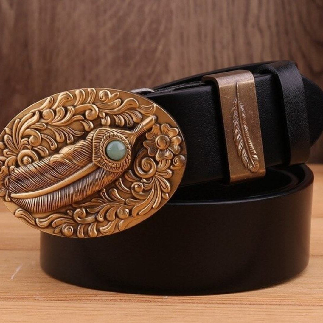 Close-up of a black leather belt with an ornate, gold-colored metal buckle featuring a feather design and a small turquoise stone.