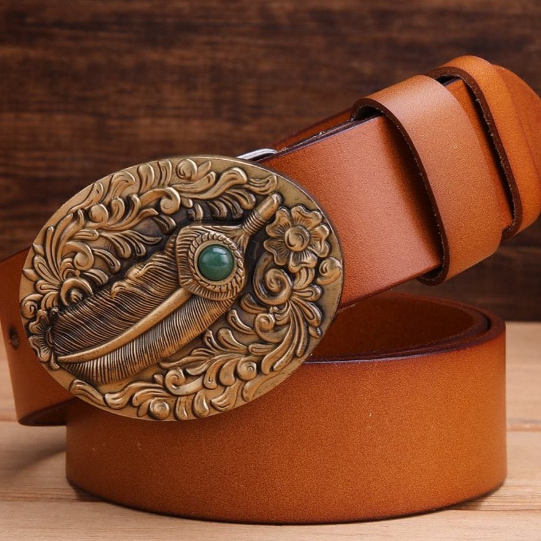 Close-up of a brown leather belt with an oval, decorative metal buckle featuring a feather and green gem.