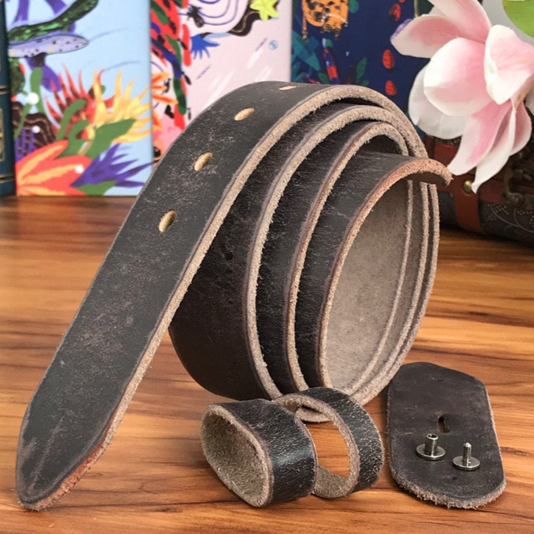 Close-up of a dark brown leather belt with silver hardware, presented on a wooden surface amidst decorative books and flowers.