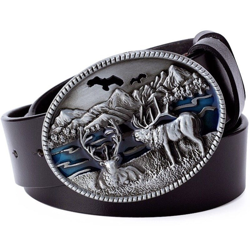 Close-up of a black leather belt with a large, oval, silver buckle depicting a landscape with two deer, mountains, and birds.
