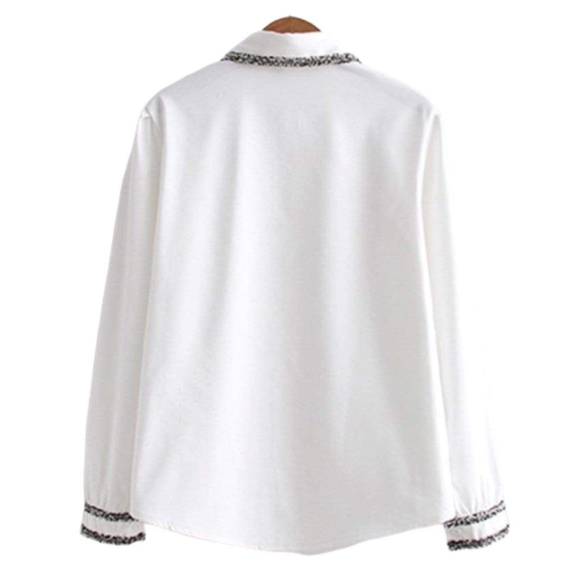 White blouse with embellished collar and cuffs hanging on a wooden hanger.
