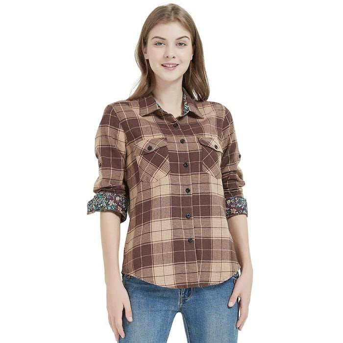 A woman wearing a brown and tan plaid shirt with floral cuffs and blue jeans.