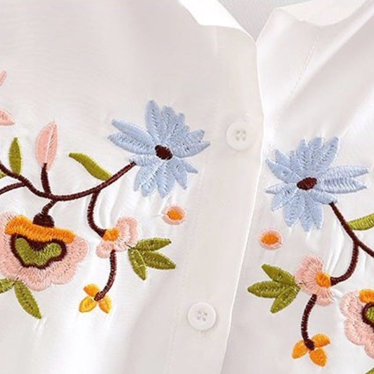 Close-up of a white blouse with floral embroidery.