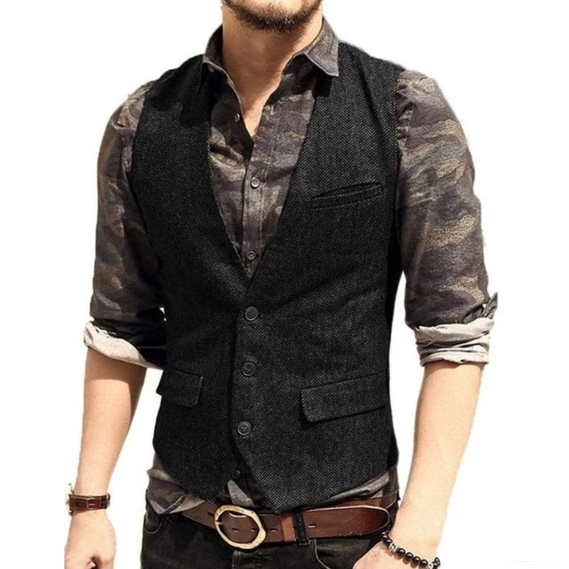A man poses in a dark herringbone vest over a patterned button-down shirt, accented by a brown leather belt and accessories.