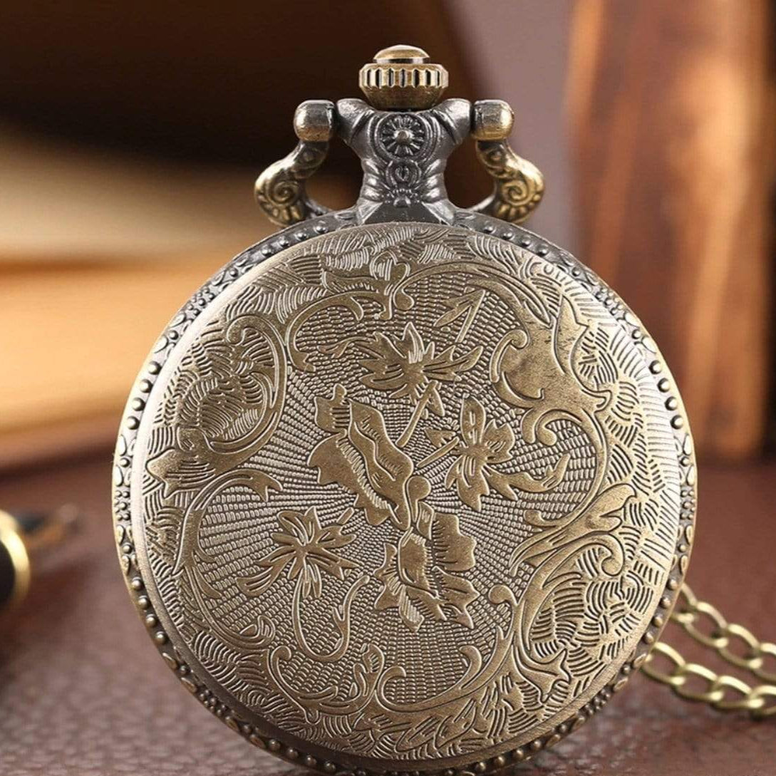 Close-up of an ornate, bronze-colored pocket watch with floral engraving. 
