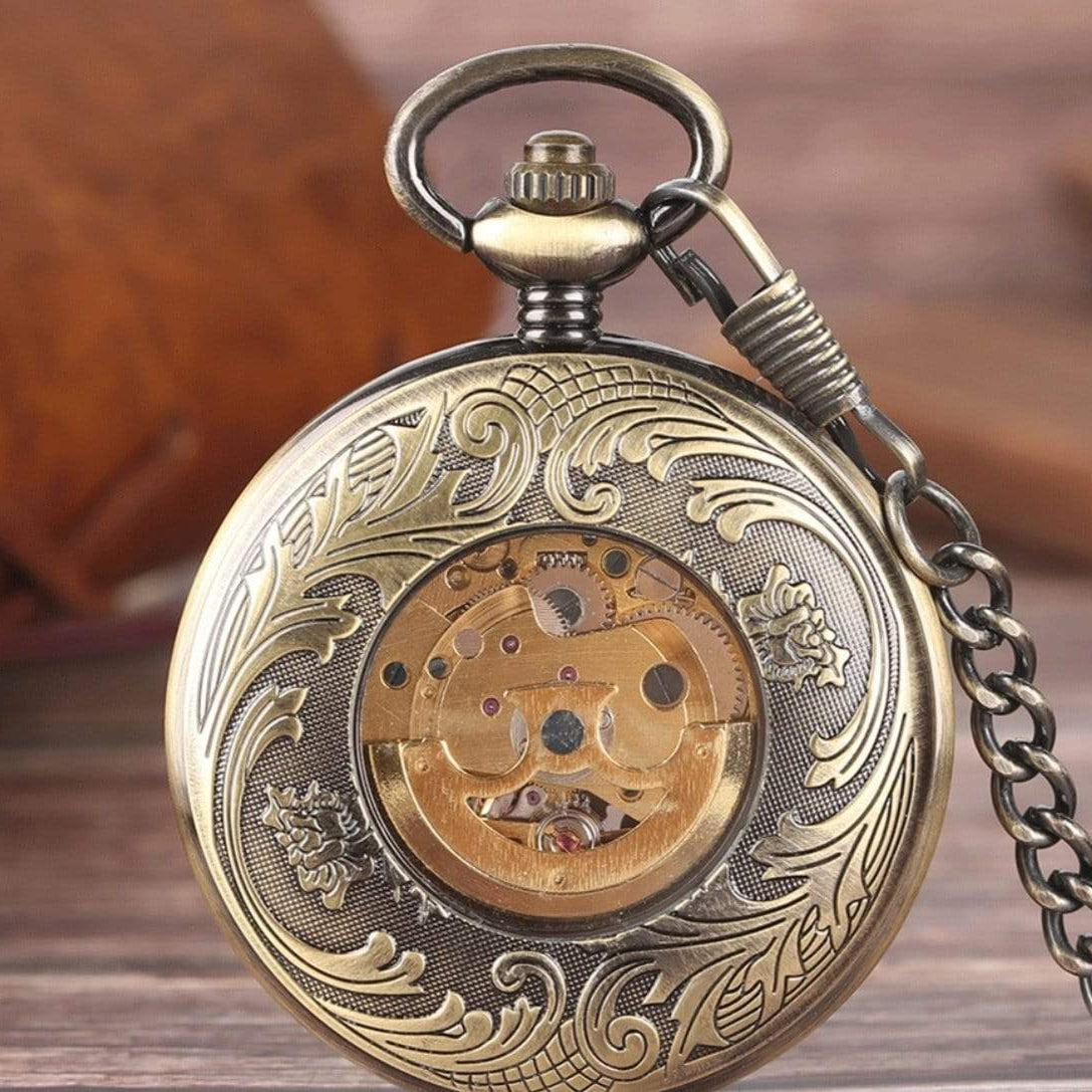 Close-up of an ornate, bronze-colored pocket watch with a visible gear mechanism and a thick chain.
