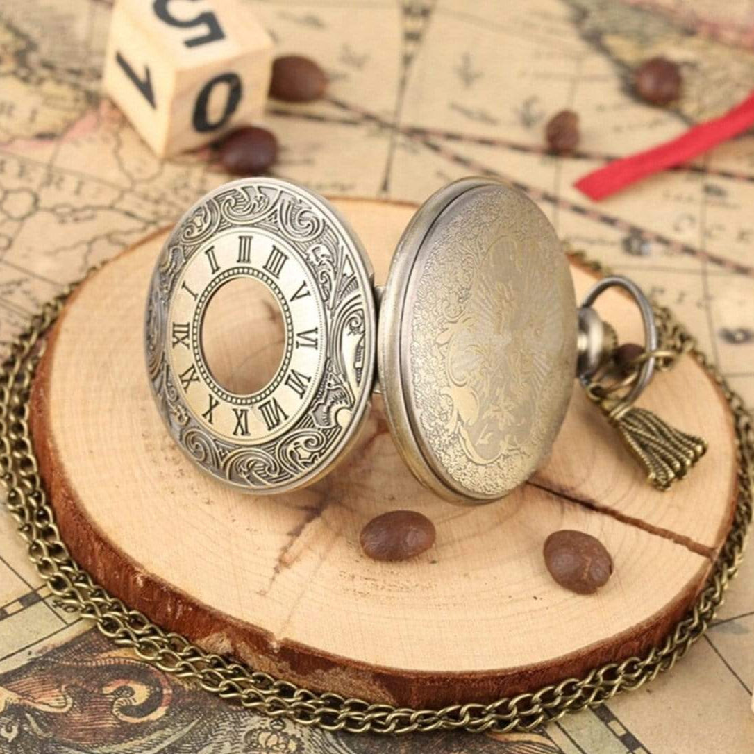 Open antique-bronze pocket watch on wooden base with chain.
