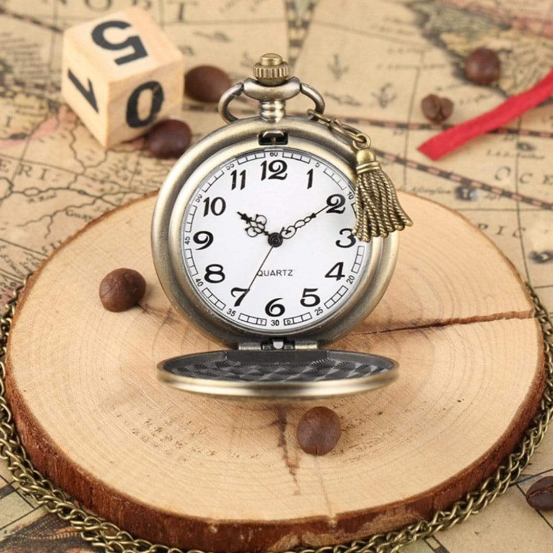 Close-up of a bronze-colored pocket watch resting on a wood slice, accented by coffee beans, atop a map, and accompanied by a dice and a red cord.