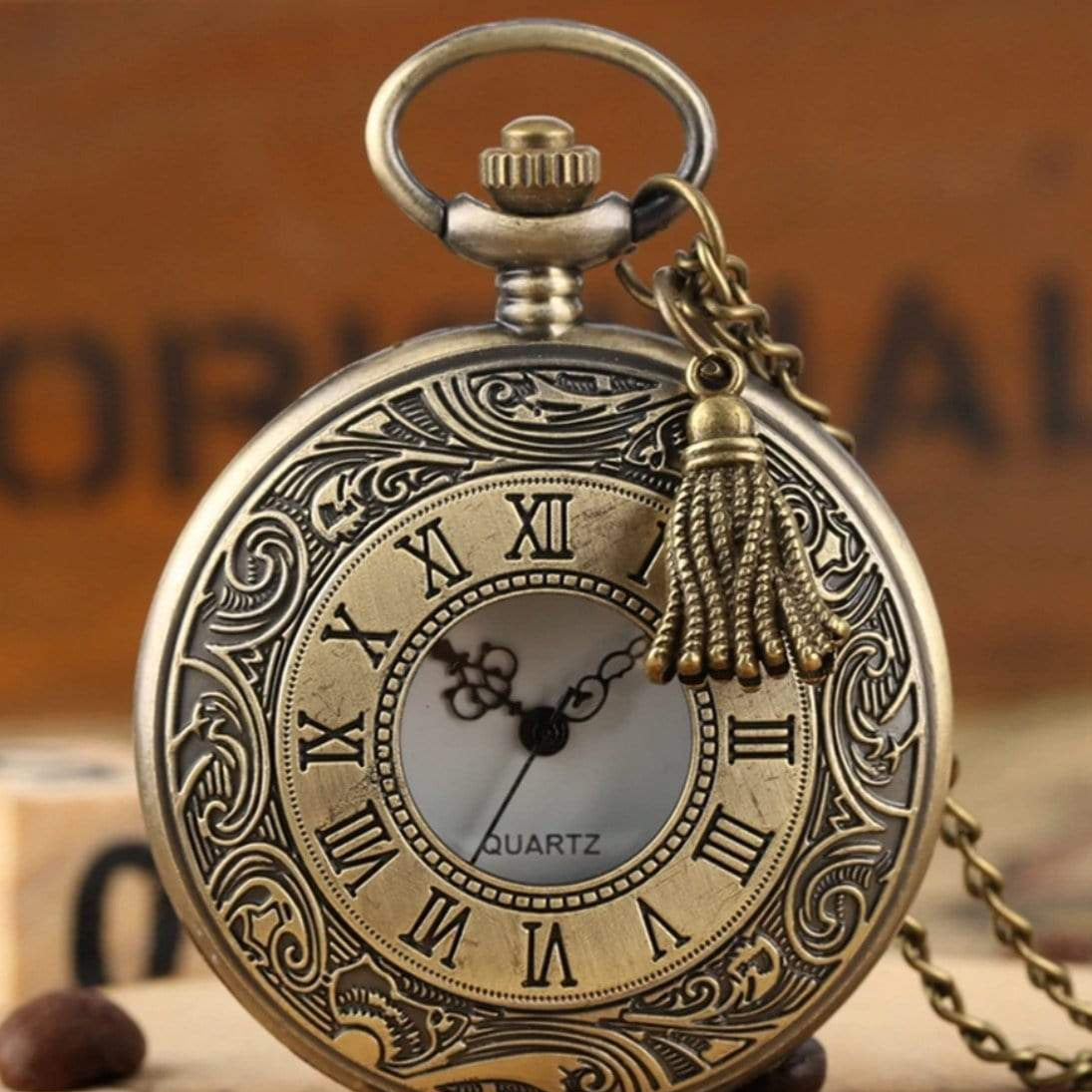 Close-up of an ornate, bronze-colored pocket watch with Roman numerals and a tassel.
