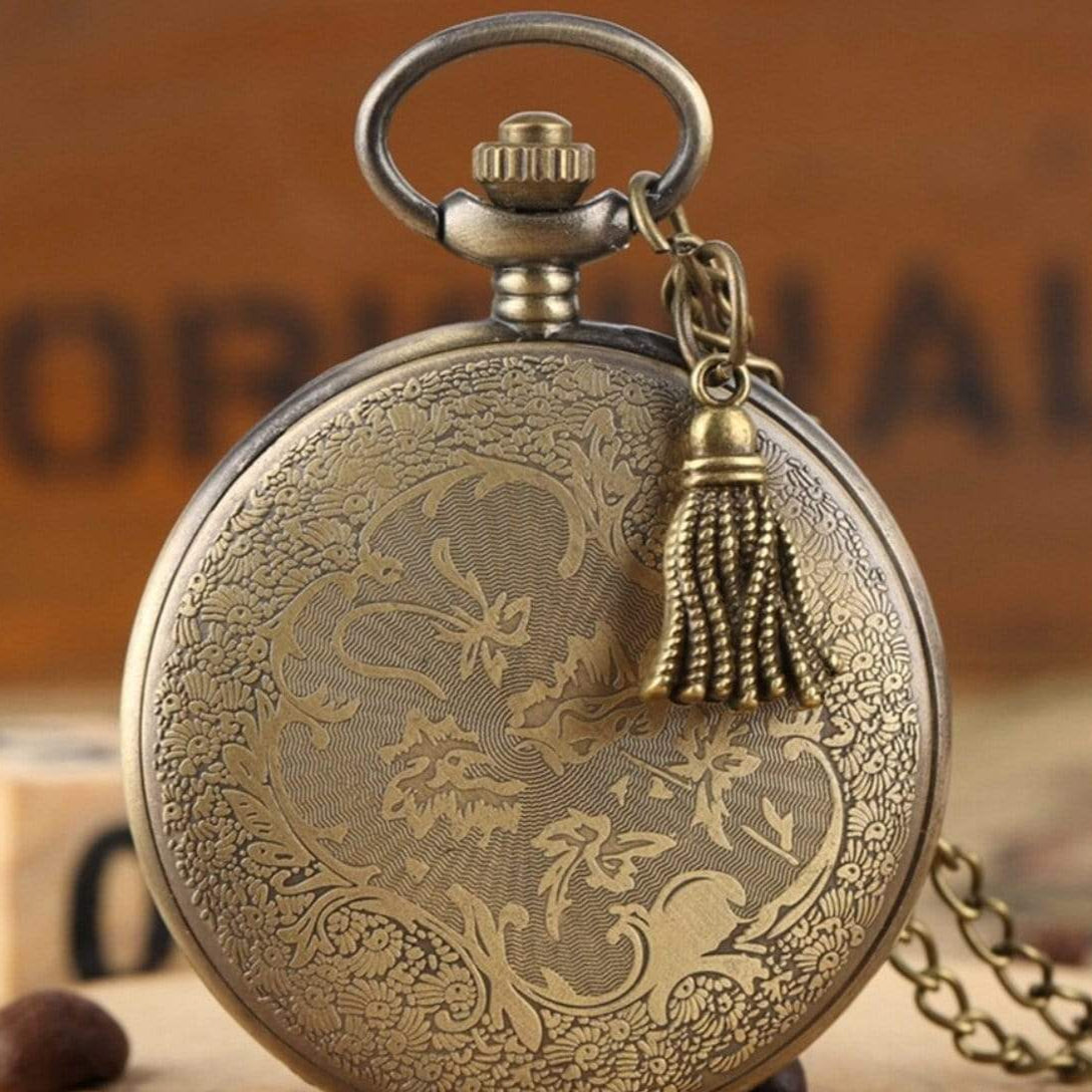 Detailed bronze pocket watch with a tassel on a wooden surface.
