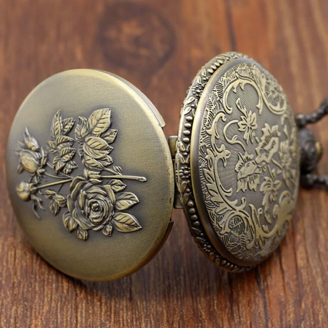 Open, antique-style bronze pocket watch with floral designs on a wooden surface.