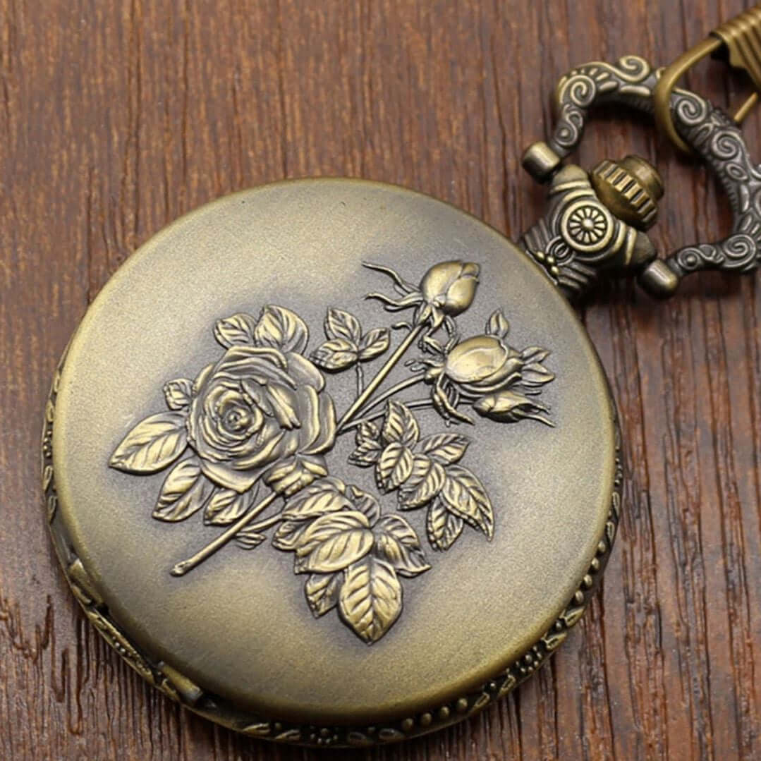 Close-up of a bronze pocket watch with raised floral design on a wooden surface.