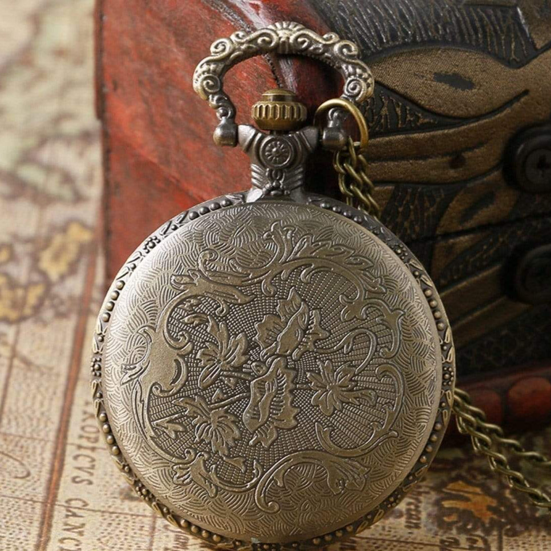 Close-up of a vintage-style, bronze pocket watch with floral engraving, on a map and next to a wooden box.