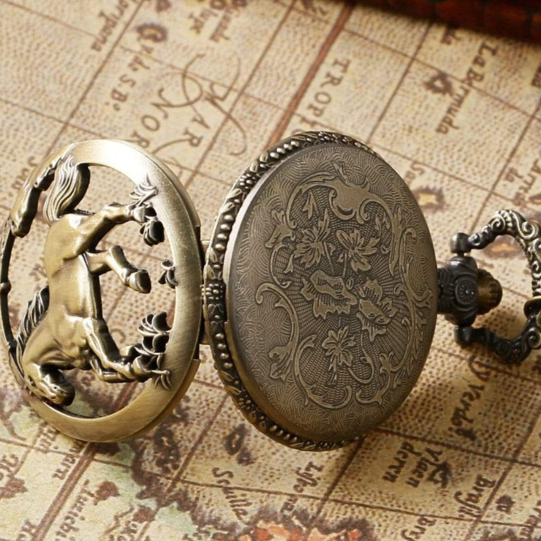 Close-up of an open, gold-colored pocket watch with a horse design on the face cover, resting on a map.