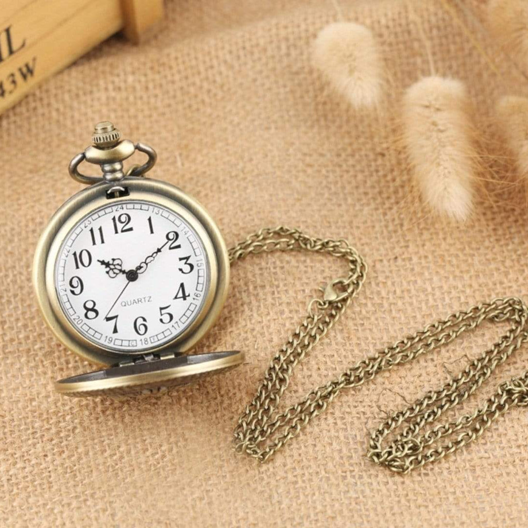 Close-up of an open, bronze-colored pocket watch with a chain on a burlap surface.