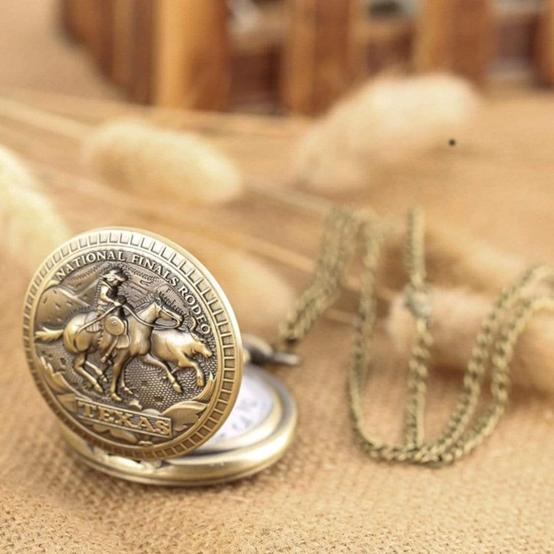 Close-up of a bronze pocket watch with a chain, featuring a cowboy riding a horse inside a circular emblem that says "National Finals Rodeo Texas".