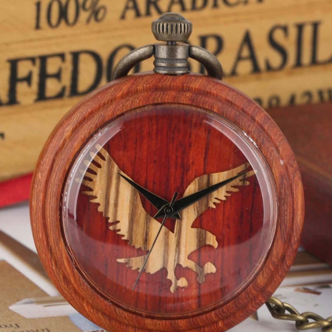 Close-up of a round, wooden pocket watch with a transparent face featuring an eagle design and black clock hands. 
