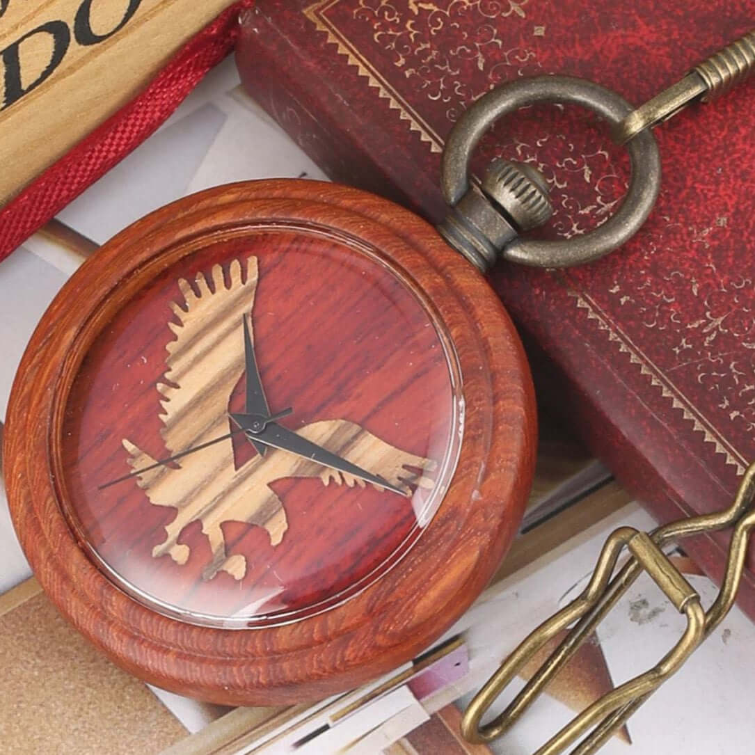 Close-up of a wooden pocket watch featuring an eagle design on a red background, chain visible.
