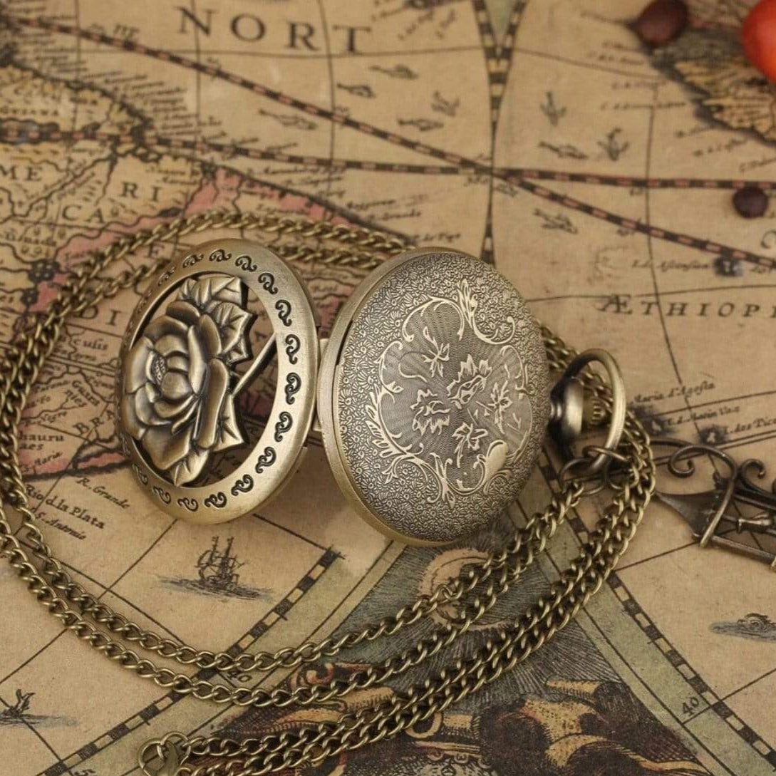 Close-up of an open antique pocket watch with a floral design and a brass chain, laying on an old map.
