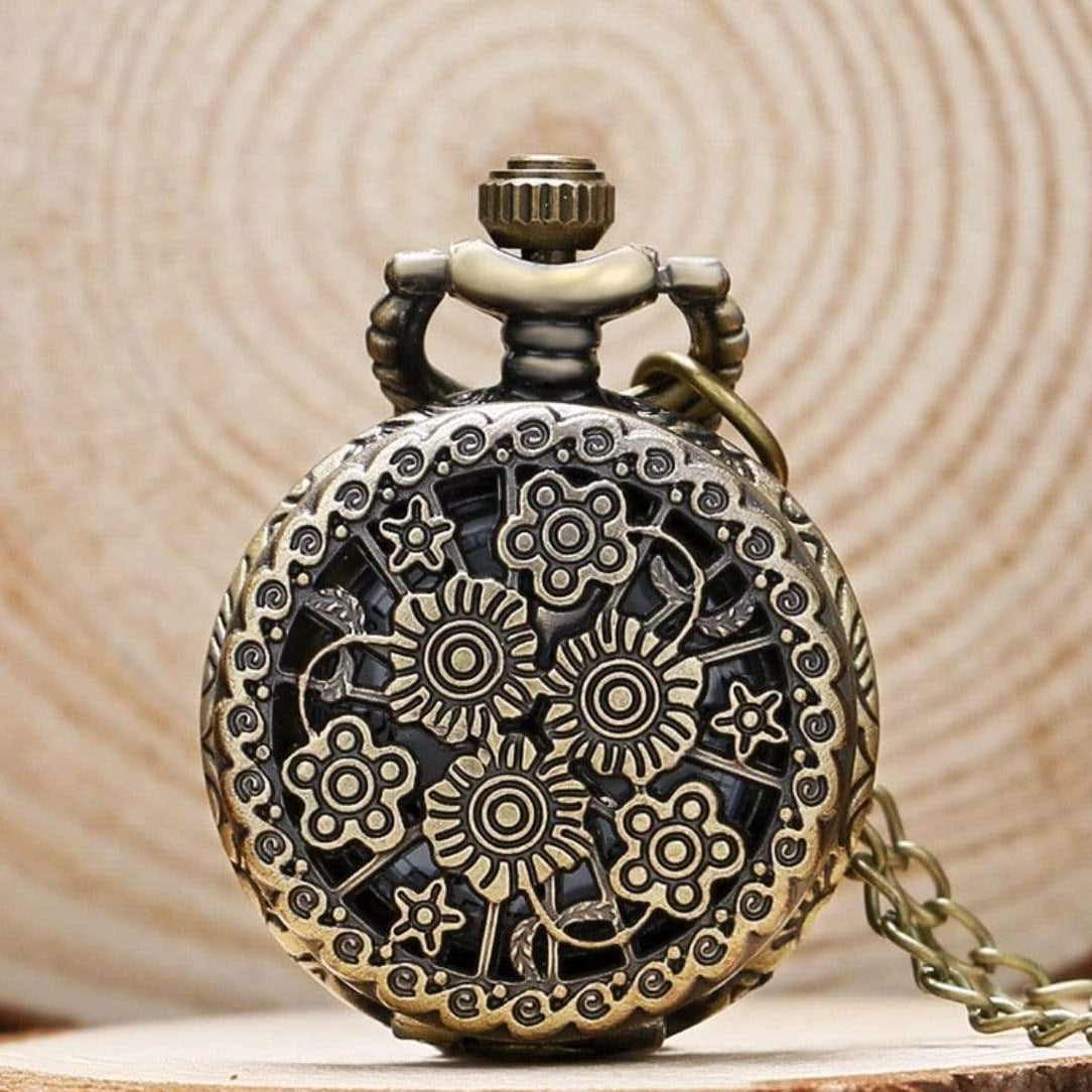 Antique, flower-embellished, bronze pocket watch on a wood surface.
