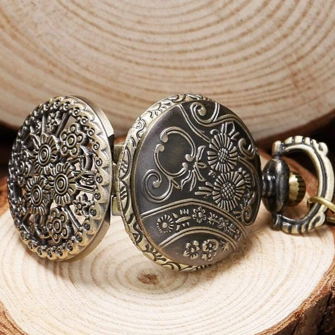 A vintage-style pocket watch with intricate floral and scroll designs, resting on a wooden surface.