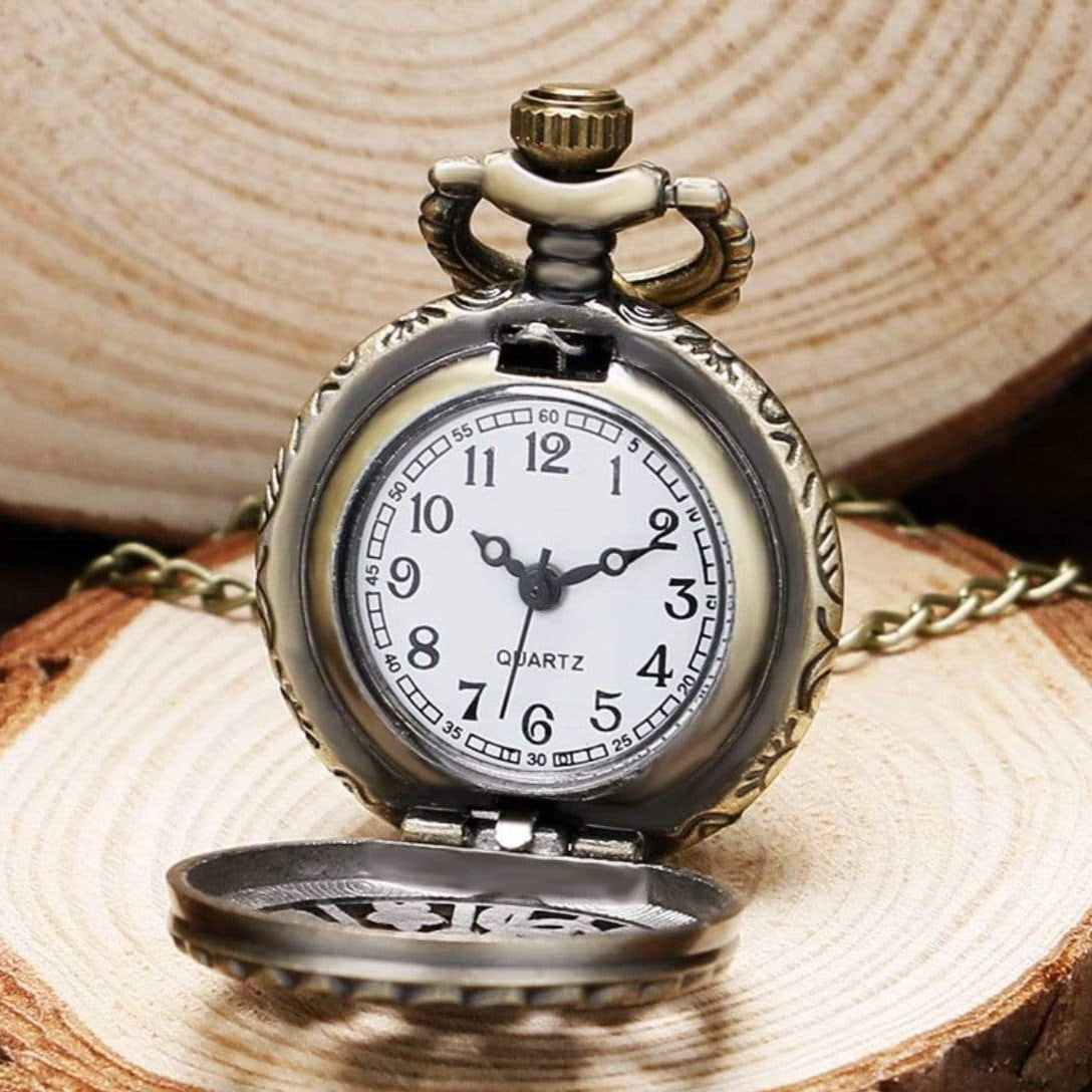 Close-up of an antique-looking bronze quartz pocket watch on a wooden surface, lid partially open.
