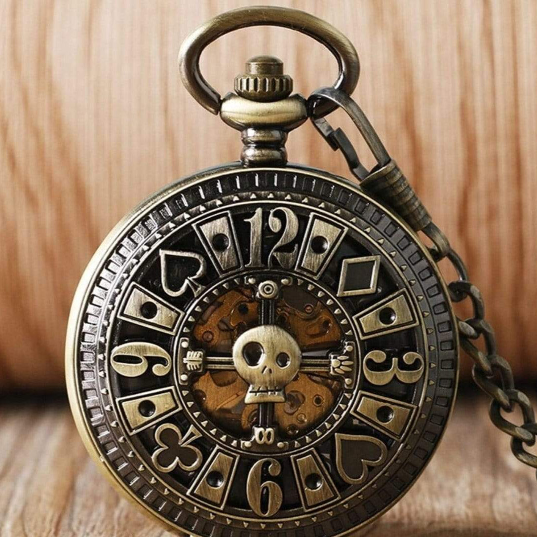 Bronze antique pocket watch with skull and playing card suit details.