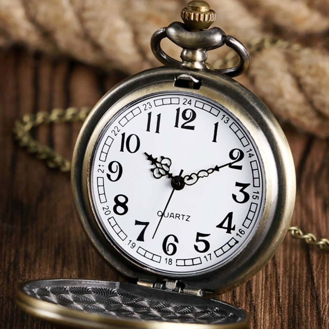 Close-up of an antique-style pocket watch with its lid partially open, displaying the watch face, chain, and ornate details against a wooden backdrop.