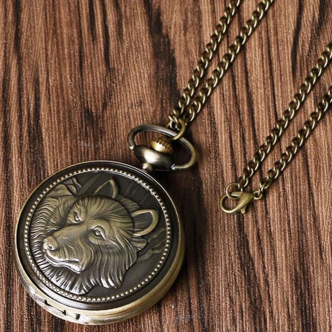 Brass-colored pocket watch with a wolf design on a wooden background.
