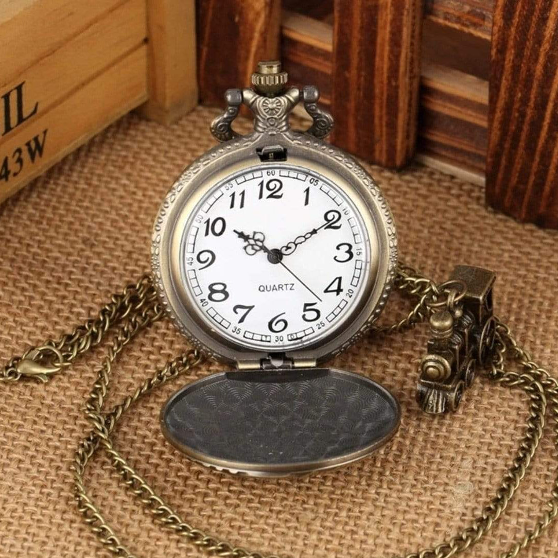 Antique bronze pocket watch with train charm on a brown burlap background.
