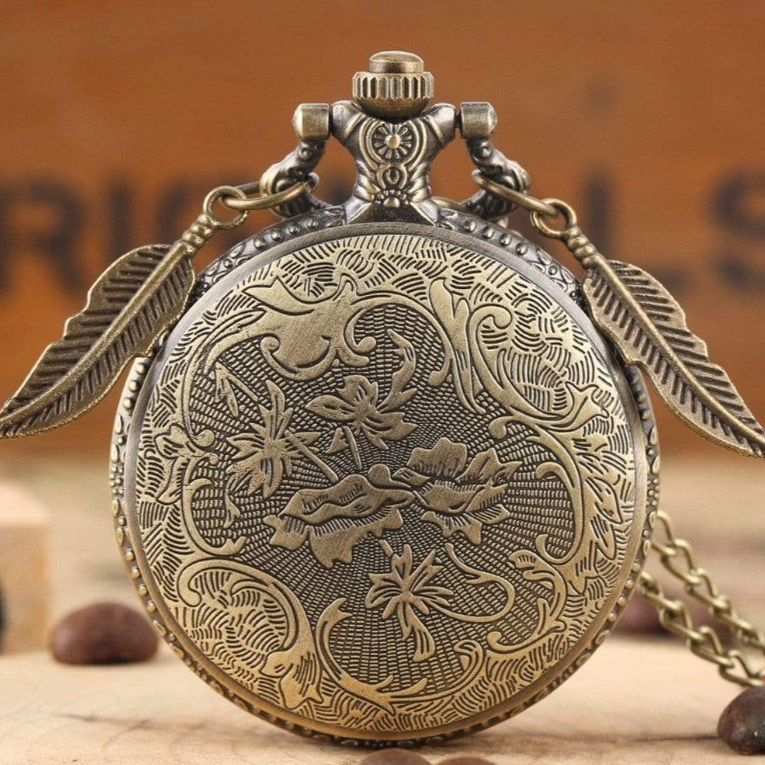 Close-up of an antique bronze pocket watch with floral engravings and feather charms, set on a wooden surface with coffee beans.