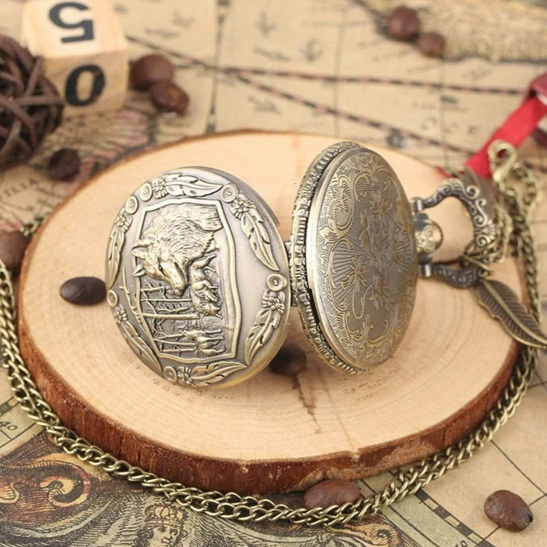 Close-up of two antique bronze pocket watches with intricate designs on a wooden base, gold chain, feather charm, and coffee beans.
