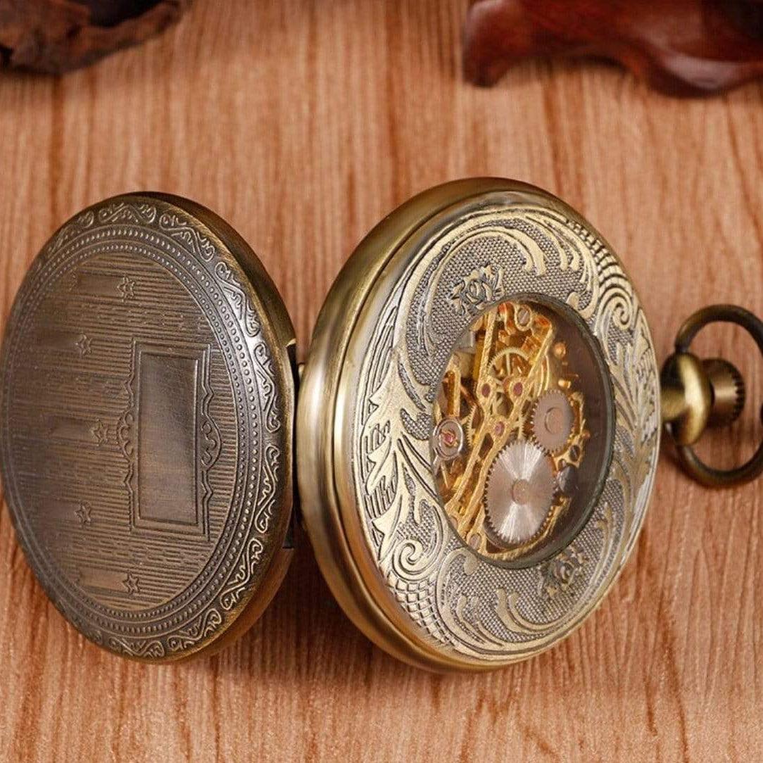 Open, ornate, gold-toned pocket watch with visible gears on a wooden surface.
