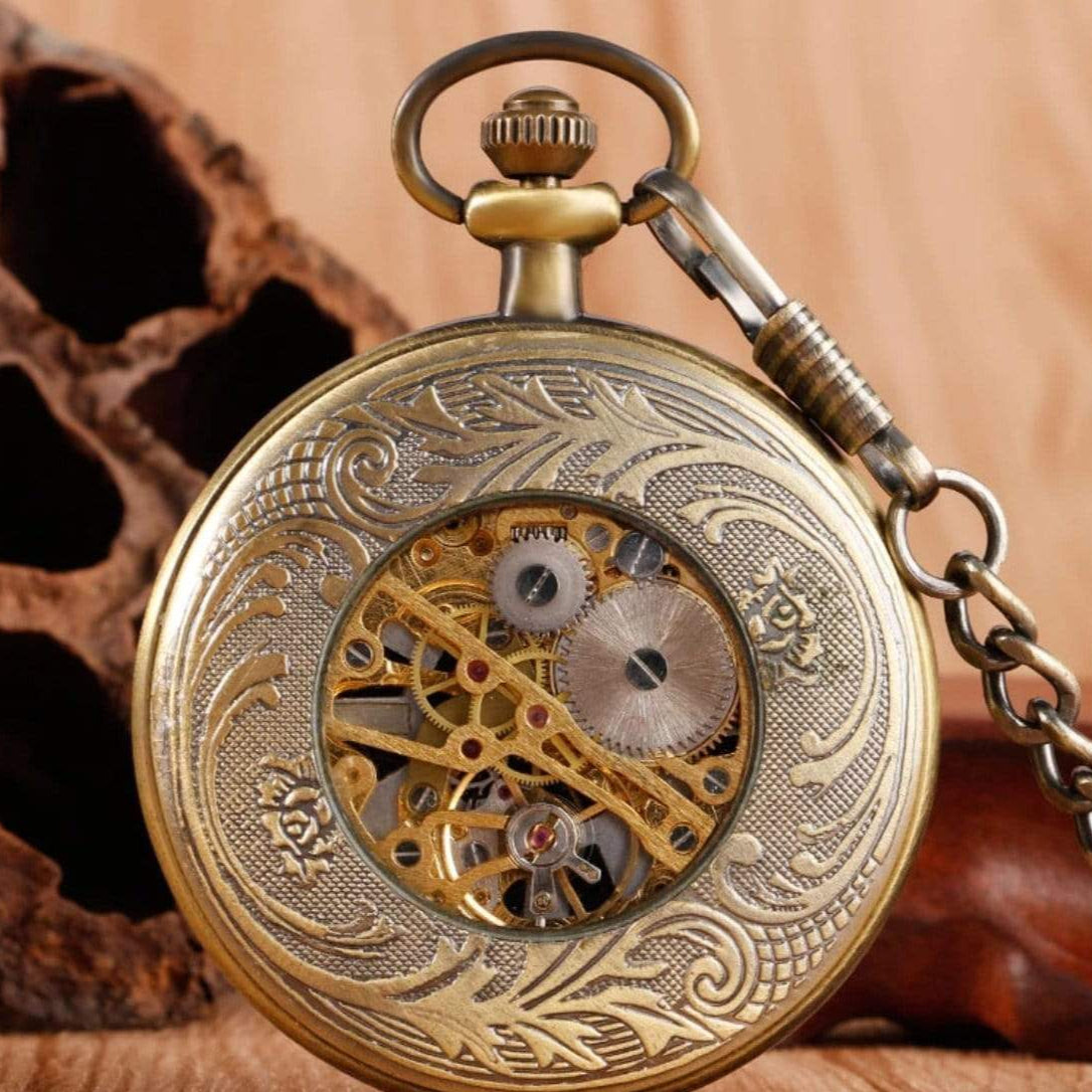 Close-up of a gold, antique-looking pocket watch with visible gears and chain. 
