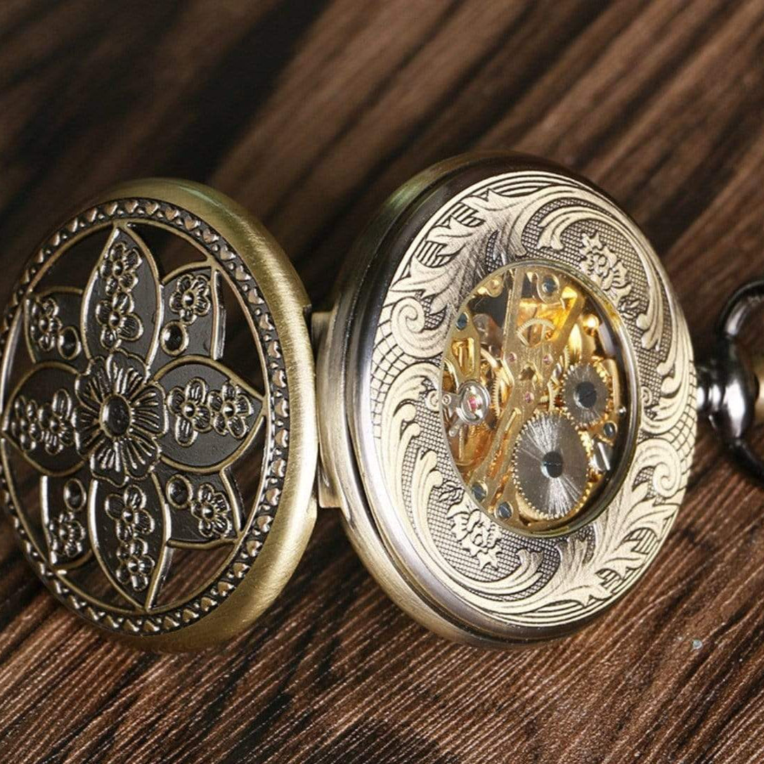 Close-up of an open, ornate, vintage pocket watch with a floral design on the lid, revealing gold gears and intricate detailing, sitting on a wooden surface.